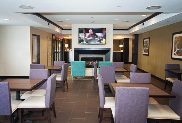 Ein Restaurant mit mehreren Tischen, Stühlen, einem an der Wand befestigten Fernseher und einem Kamin.