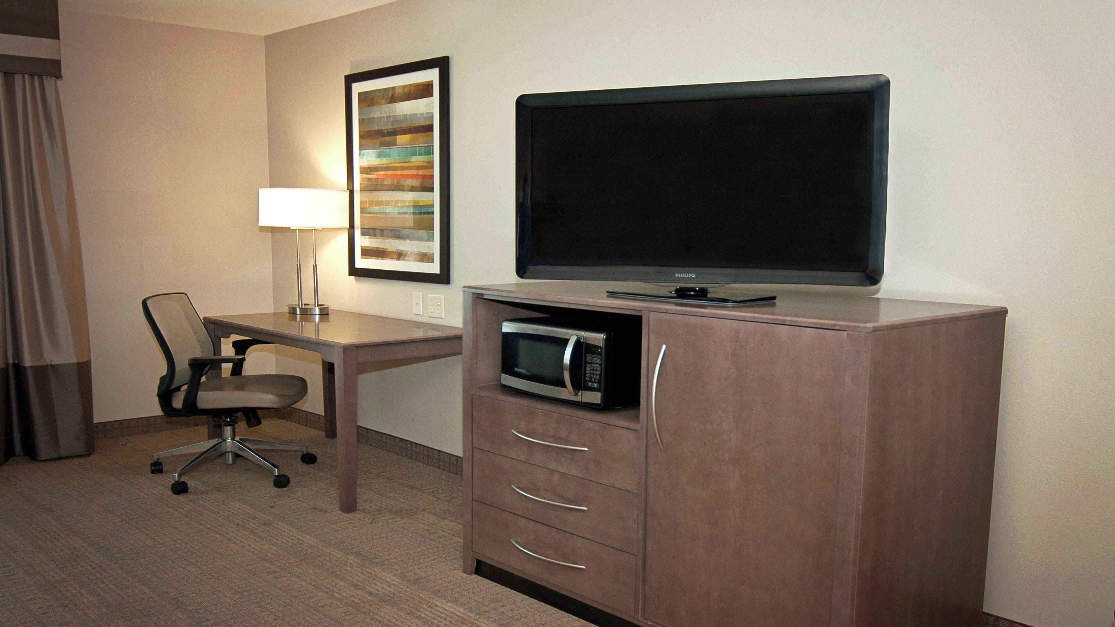 A hotel room with a desk, a chair, a television, a microwave, and a framed picture on the wall.