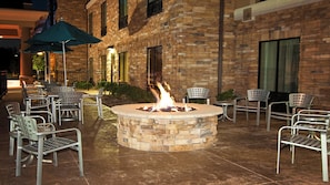 An outdoor seating area with a fire pit surrounded by metal chairs and tables, set against a brick building facade. - Holiday Inn Express & Suites Wichita Northeast by IHG (Wichita)