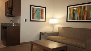 A modern living room with a sofa, coffee table, and a kitchen area with a microwave. There are two framed artworks on the wall.