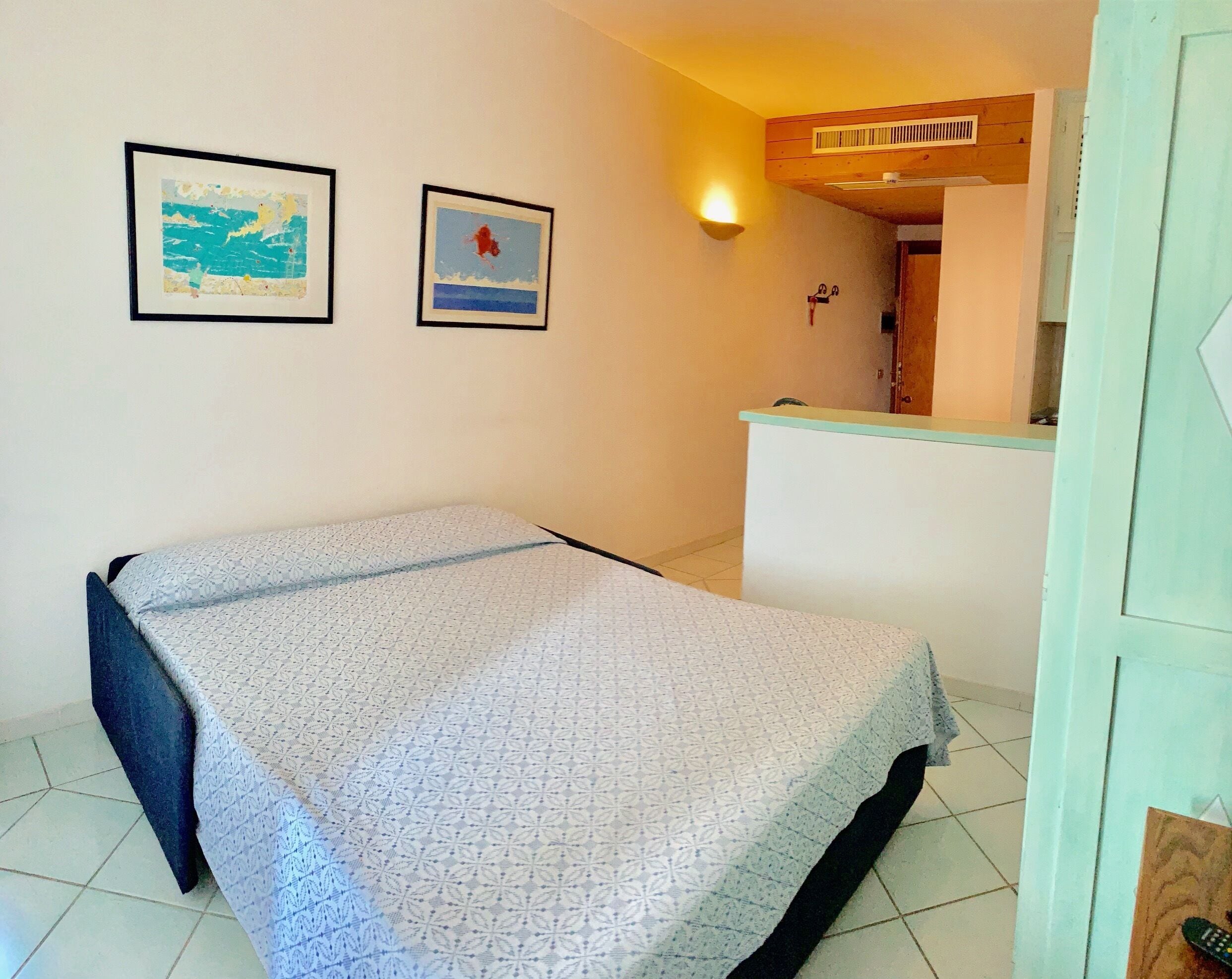 Um quarto pequeno com uma cama, uma escrivaninha e duas imagens emolduradas na parede.