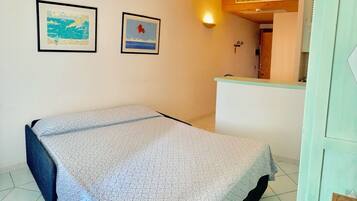 Um quarto pequeno com uma cama, uma escrivaninha e duas imagens emolduradas na parede.