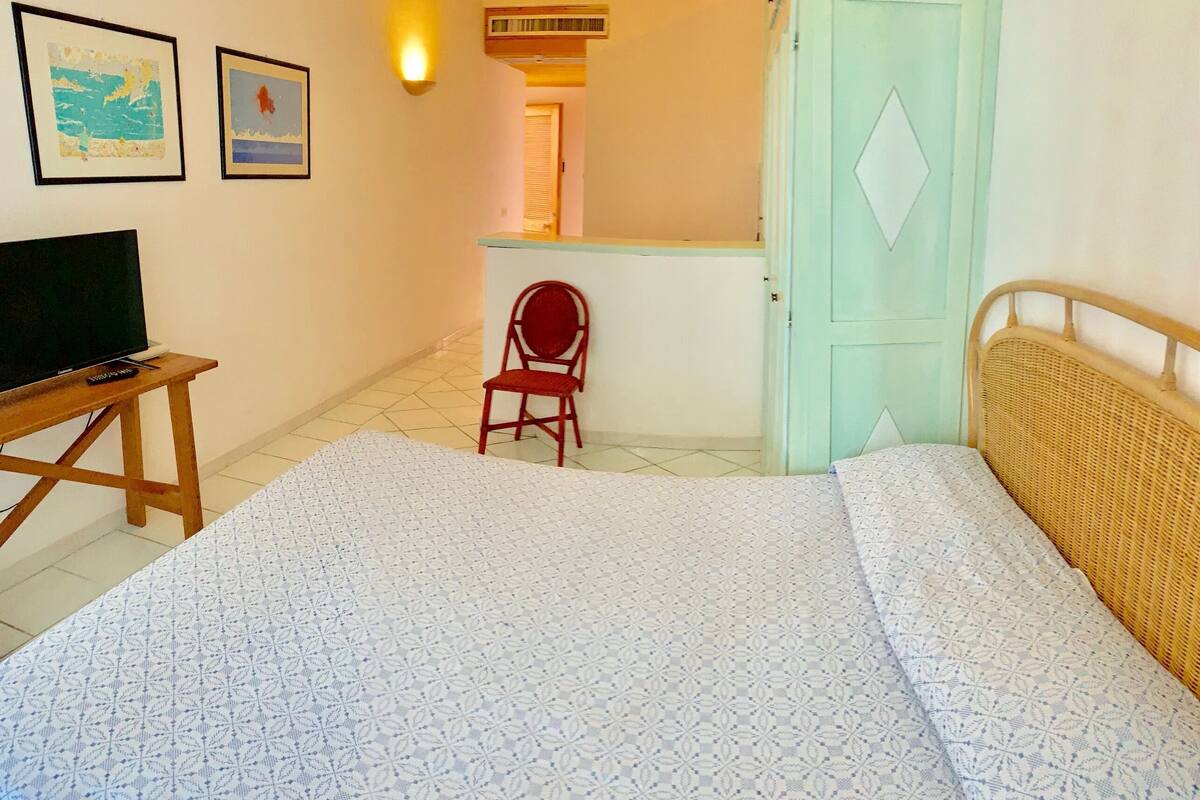 Een slaapkamer met een bed, een stoel, een tv op een meubelstuk en twee ingelijste foto's aan de muur.