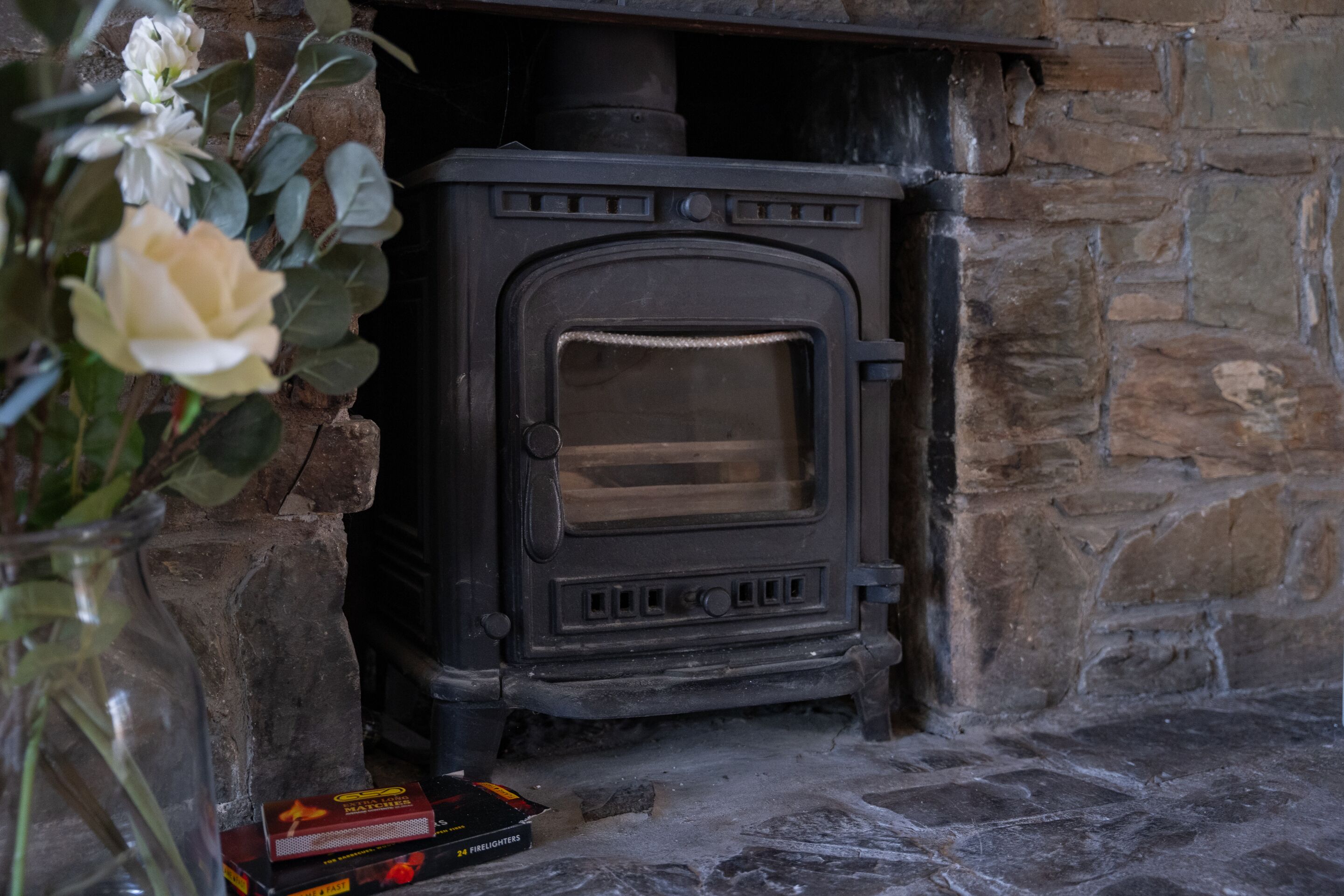 A stone fireplace with a wood-burning stove, a firebox, and a fireguard.