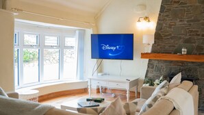 Una sala de estar con un televisor de pantalla plana mostrando 'Disney 10', una chimenea de piedra, un escritorio blanco y un sofá color beige.