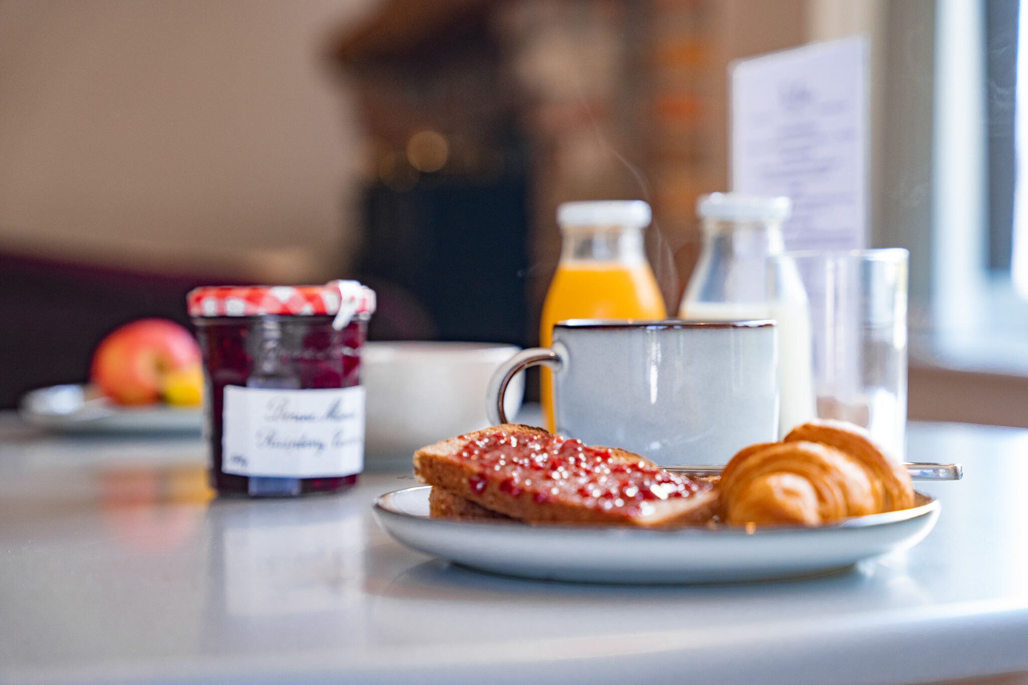 A breakfast setting with toast, jam, a croissant, a glass of orange juice, and a bottle of milk.