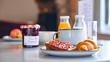 A breakfast setting with toast, jam, a croissant, a glass of orange juice, and a bottle of milk.