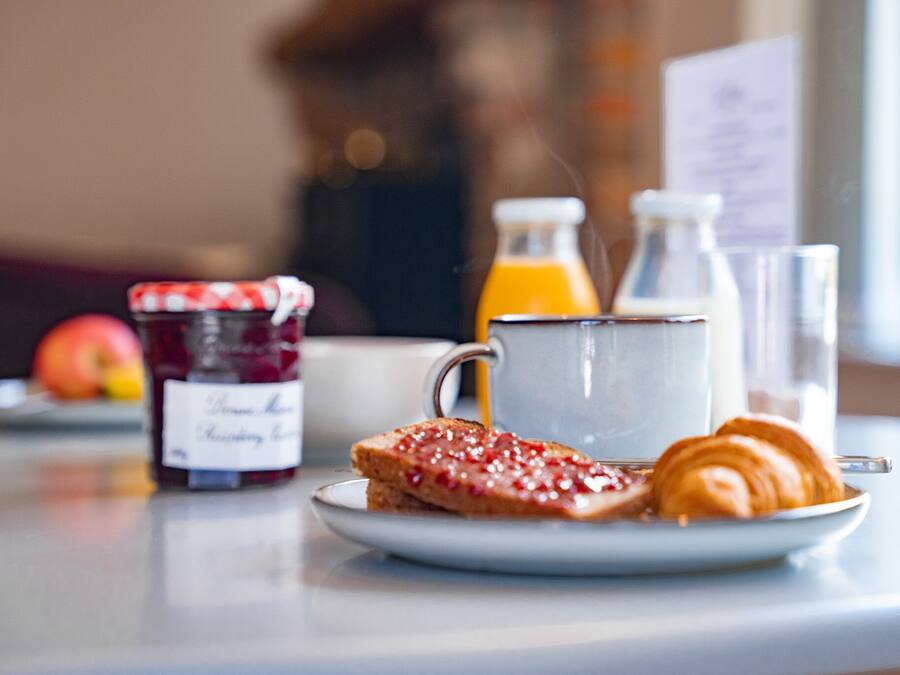 A breakfast setting with toast, jam, a croissant, a glass of orange juice, and a bottle of milk.