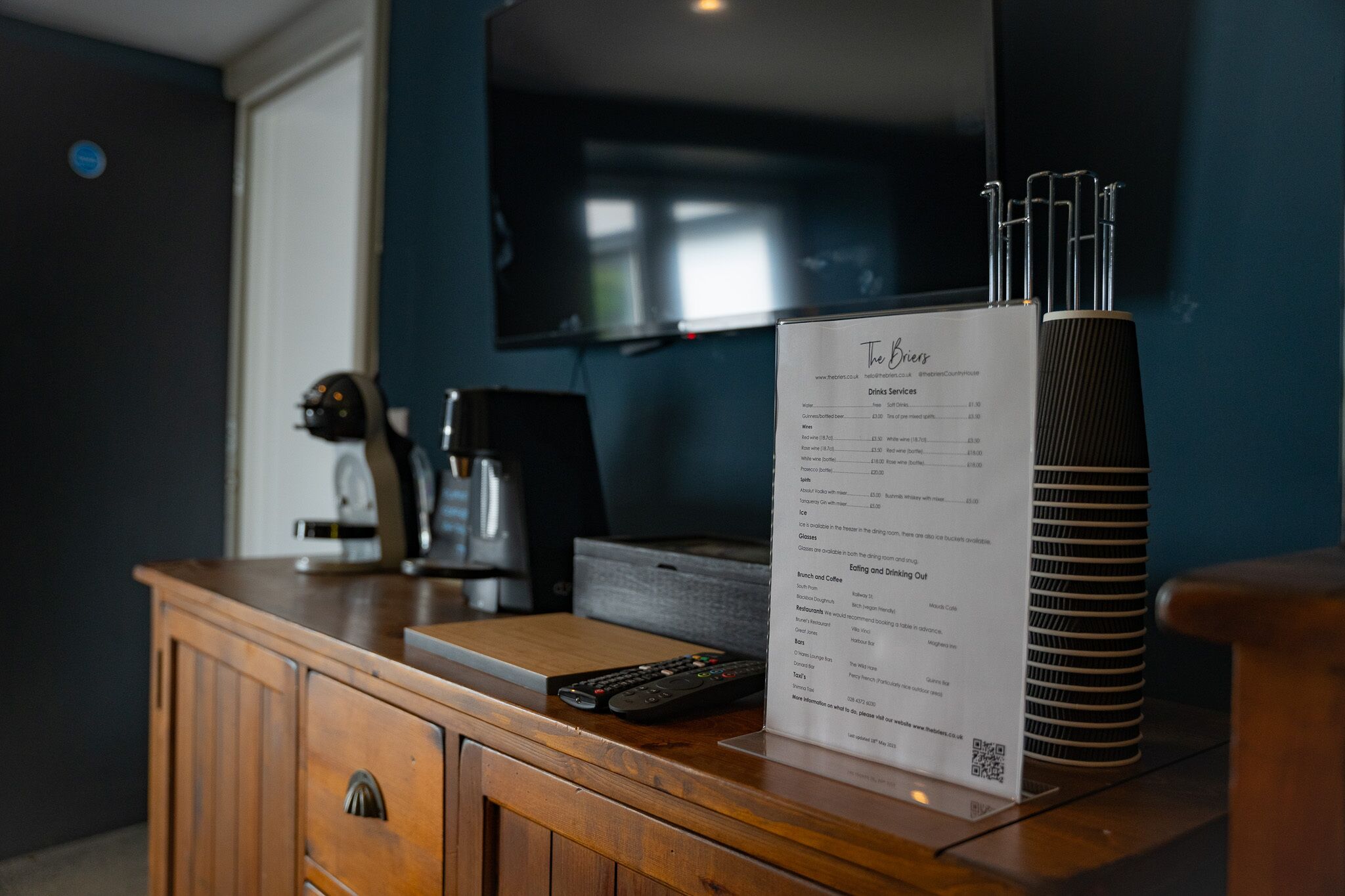A wooden counter with a menu, a remote control, and a stack of coasters.