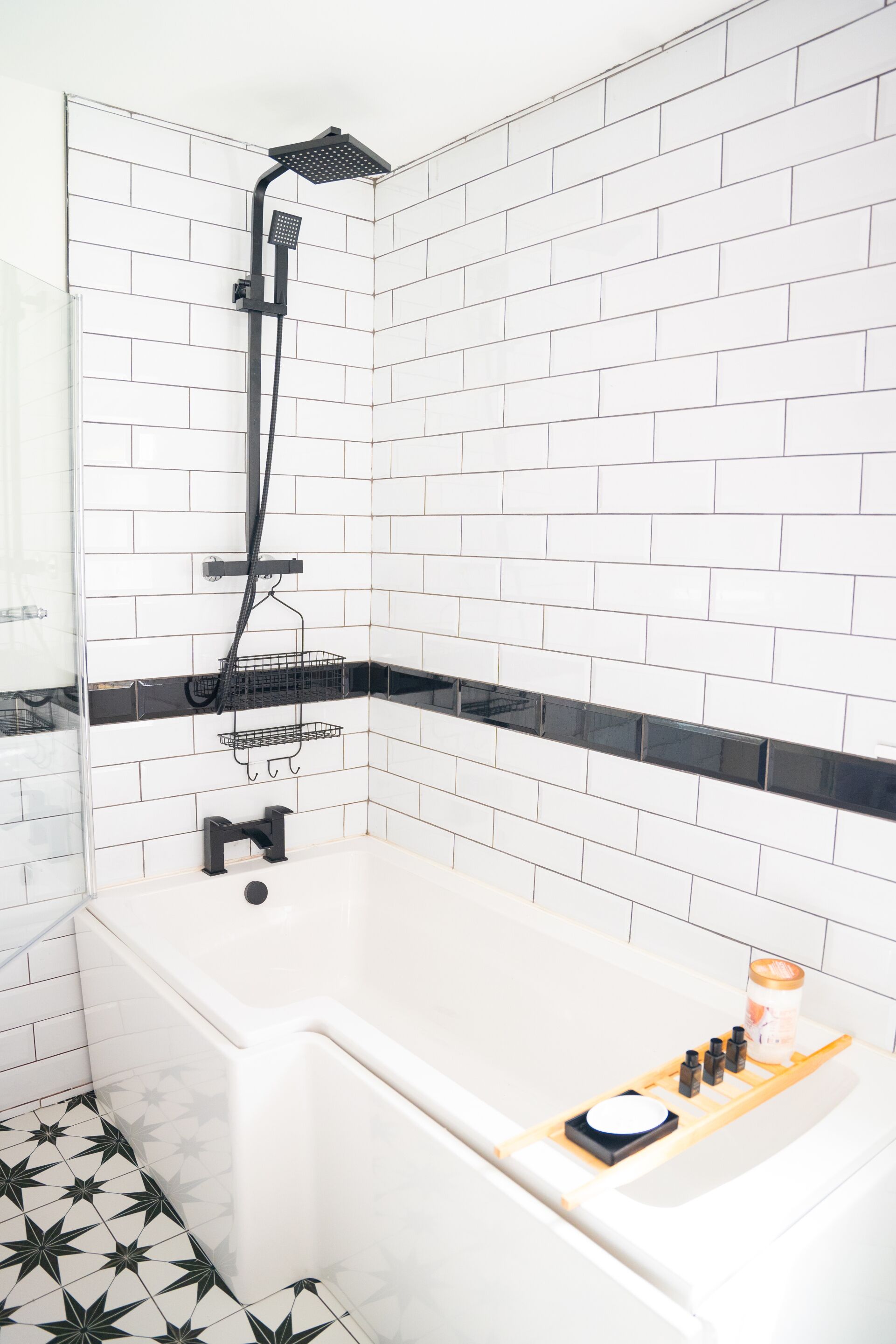 A modern bathroom with a white bathtub, black showerhead, and a tiled floor with a black and white pattern.