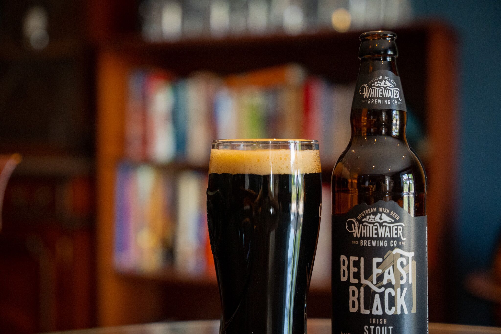 A glass of dark beer and a bottle labeled "Whitewater Belfast Black Irish Stout" in a bar setting.