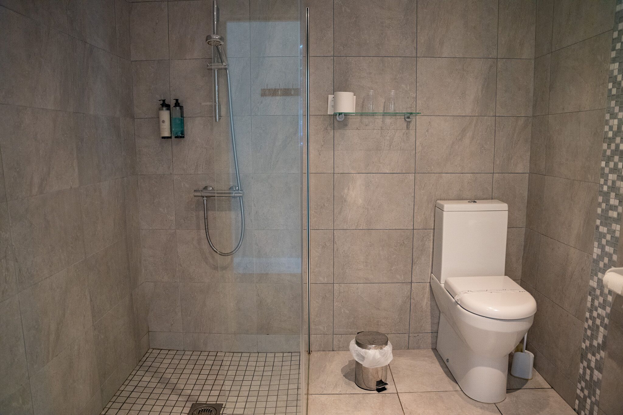 Moderni kylpyhuone, jossa on lasiseinällä varustettu suihku, wc ja pieni roskakori.