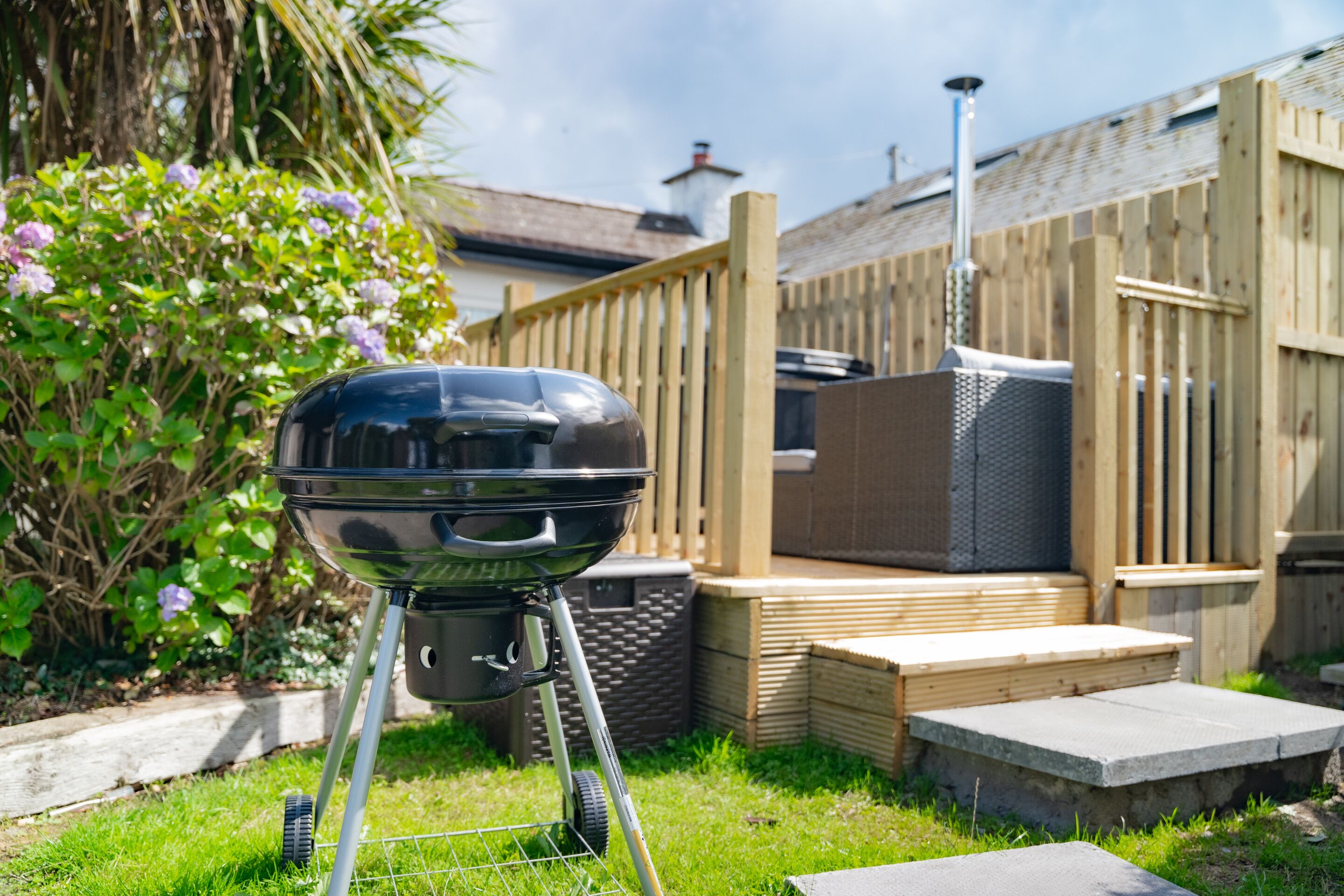 A barbecue grill in a backyard with a wooden fence, a patio, and a chimney in the background.