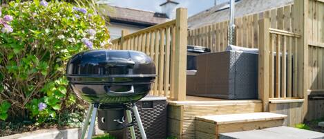 A barbecue grill in a backyard with a wooden fence, a patio, and a chimney in the background.