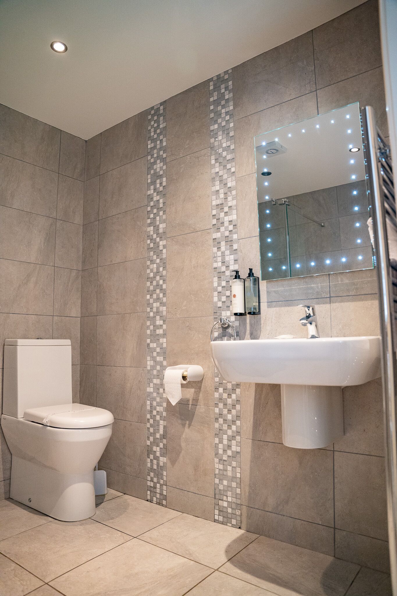 Une salle de bain moderne équipée de toilettes, d’un lavabo et d’un miroir avec éclairage.