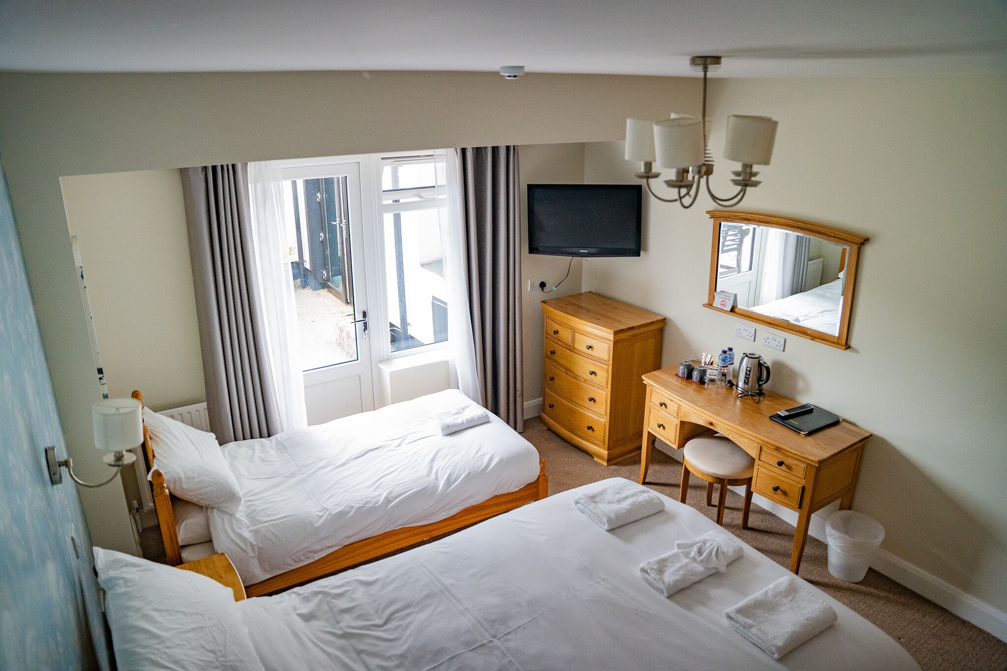 A hotel room with two beds, a desk with a chair, a television, a dresser, and a large window with curtains.