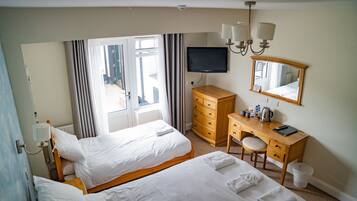 A hotel room with two beds, a desk with a chair, a television, a dresser, and a large window with curtains.