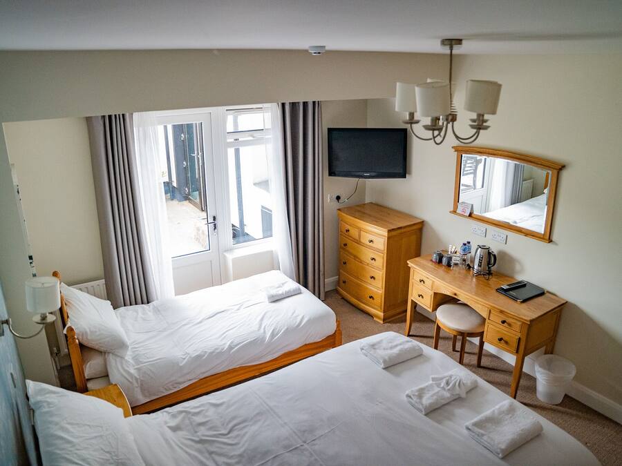 A hotel room with two beds, a desk with a chair, a television, a dresser, and a large window with curtains.