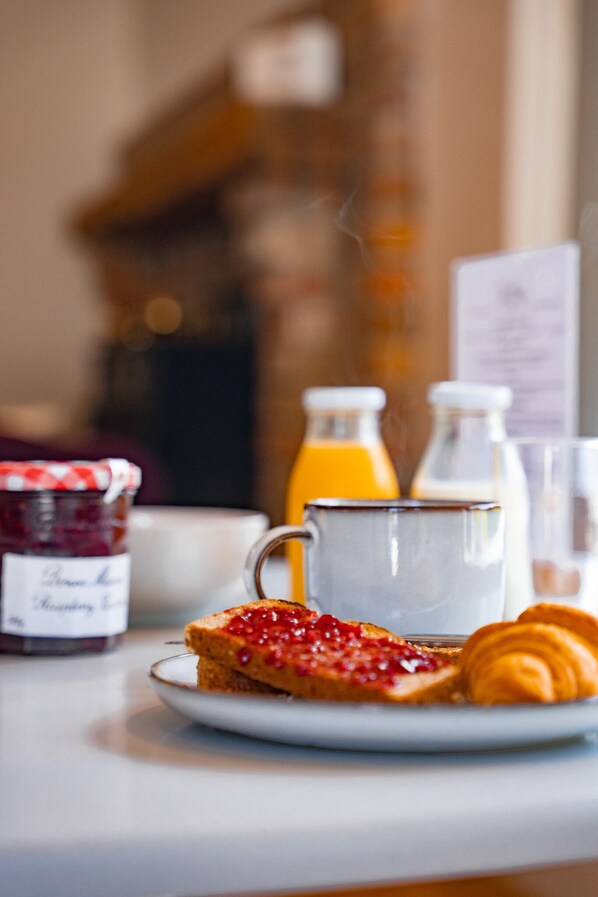 A breakfast table with a glass of orange juice, a glass of milk, a jar of jam, a plate with toast and a croissant. - The Briers (Newcastle)