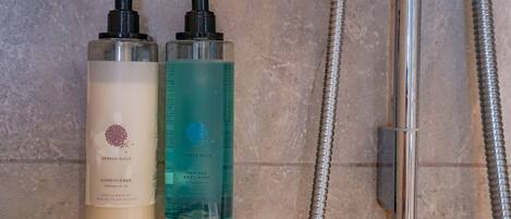 Two bottles of Geneva Guild hair and body wash next to a shower hose.