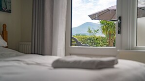Un dormitorio con una cama, una ventana y vistas a una montaña y palmeras.