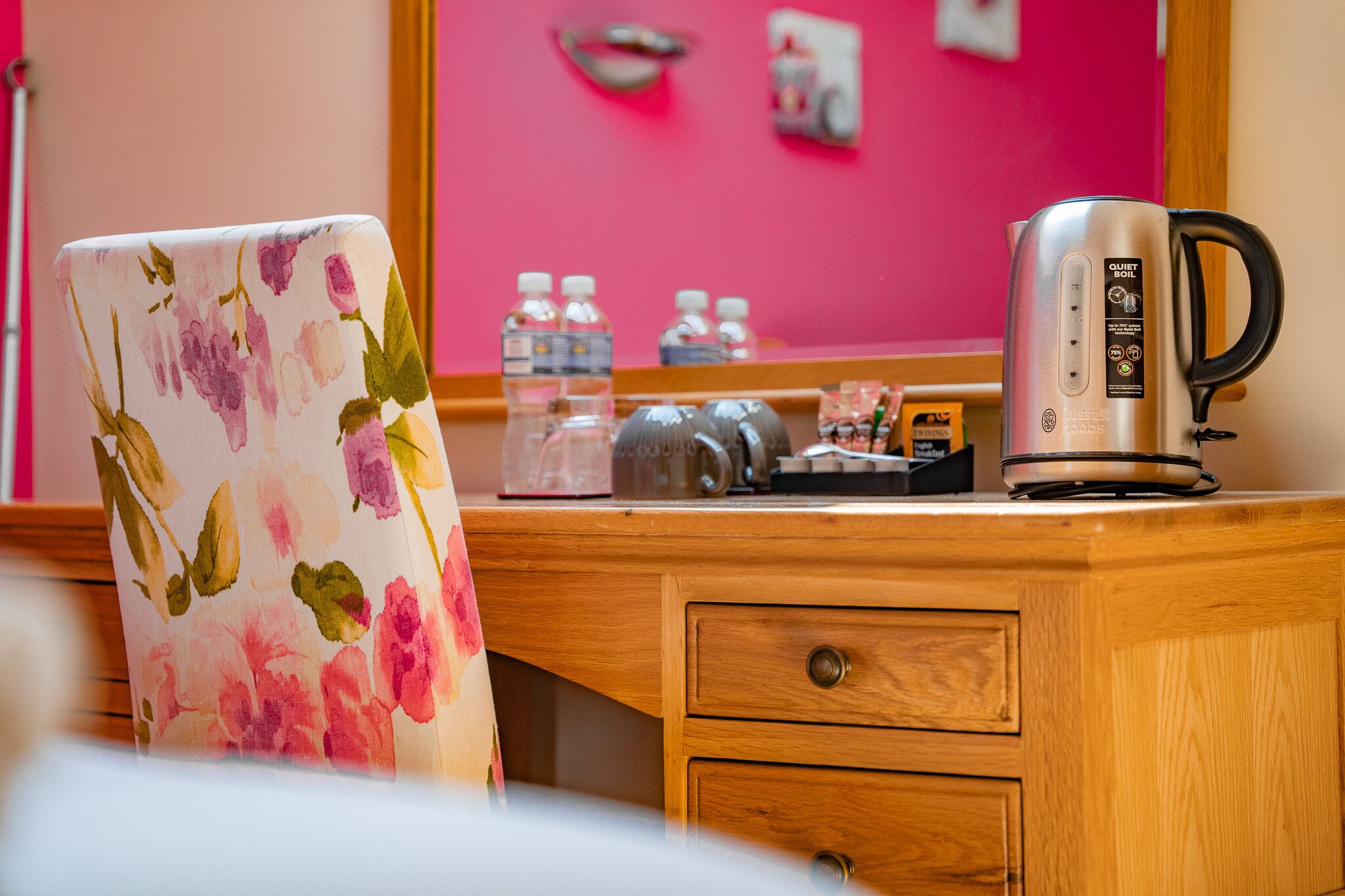 A wooden desk with a kettle, water bottles, and a floral chair.