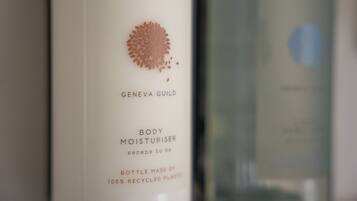A bottle of Geneva Guild body moisturizer with a floral design and text indicating it is made of 100% recycled plastic.