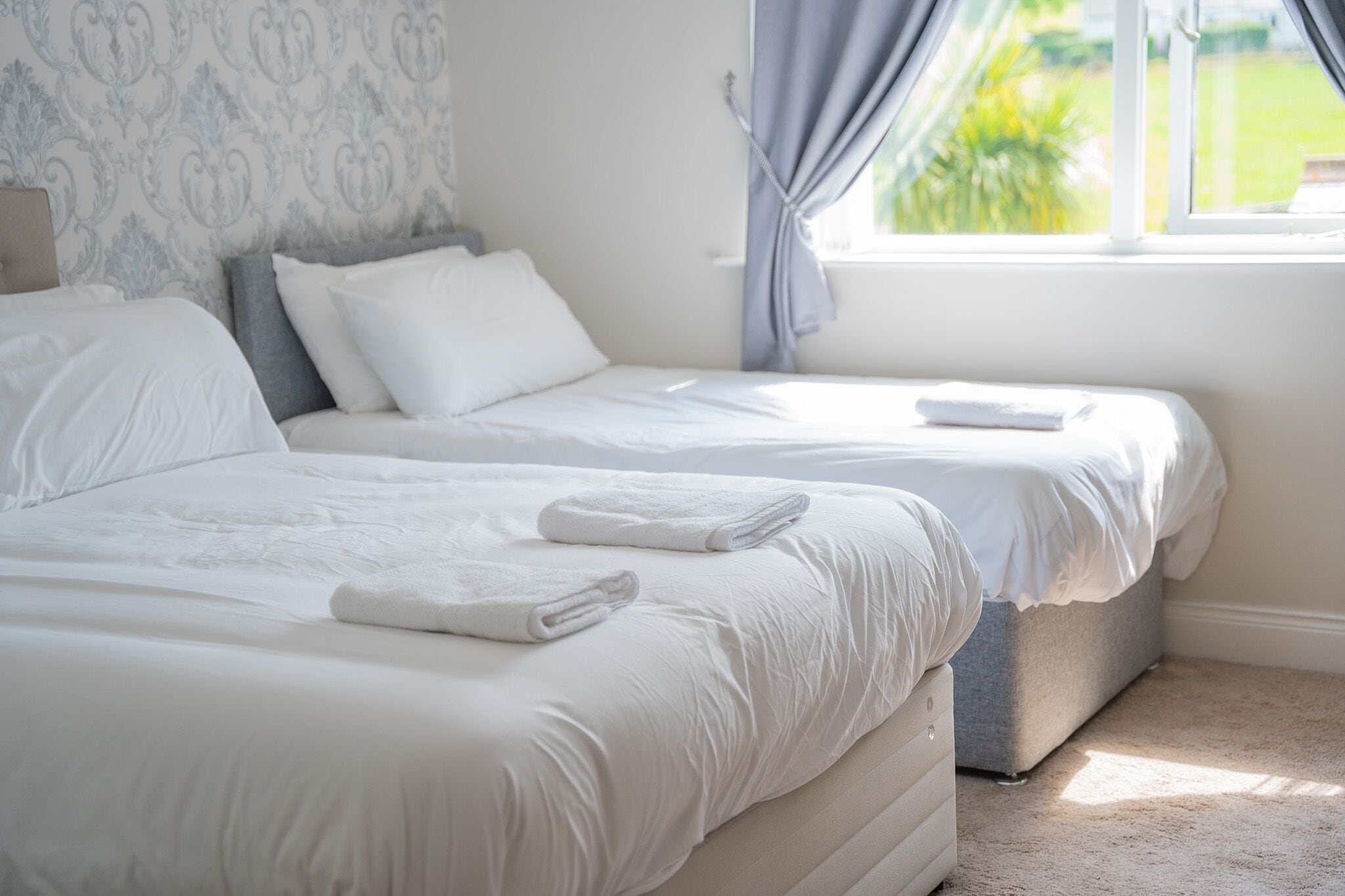 A hotel room with two beds, a window with curtains, and a patterned wallpaper.
