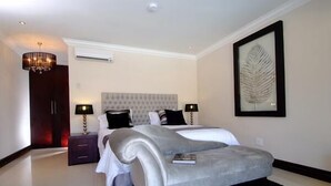 A modern bedroom with a large bed, two bedside tables, a chandelier, and a framed leaf artwork on the wall. - Sanchia Luxury Guesthouse (Durban North)