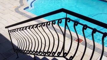 Une piscine dont le bord est revêtu de carrelage et qui est entourée d’une rambarde en métal noir.
