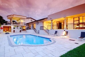A modern house with a swimming pool, outdoor seating, and a well-lit balcony.