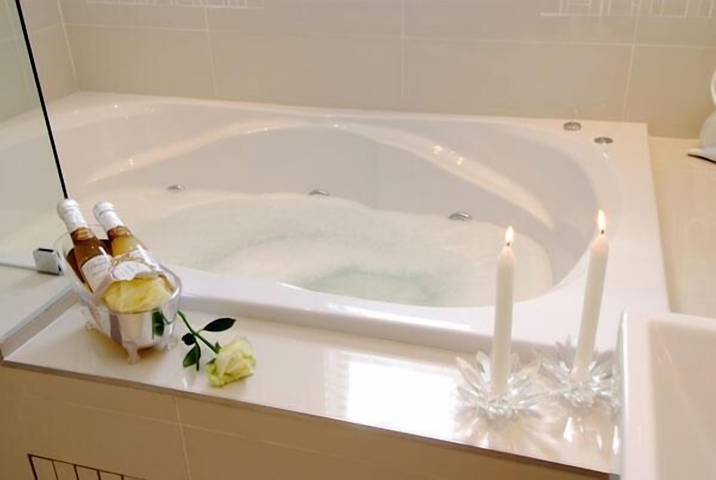 A bathtub with a bottle of champagne and a candle.