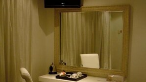 A hotel room with a bed, a chair, a desk with a flat-screen TV, a mirror, and a window with curtains. - Sanchia Luxury Guesthouse (Durban North)