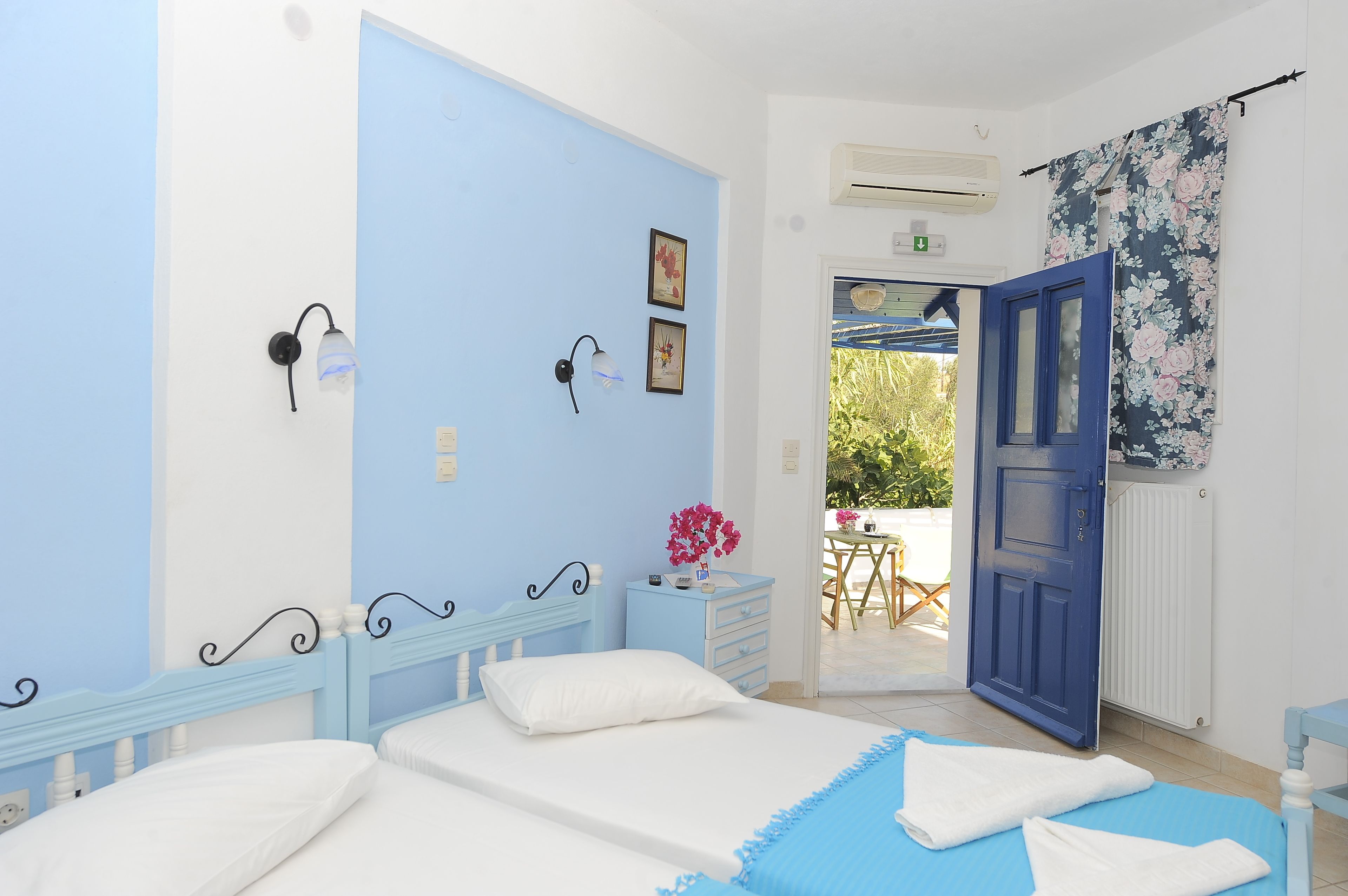 A bedroom with two beds, a blue door, and a view of an outdoor area.