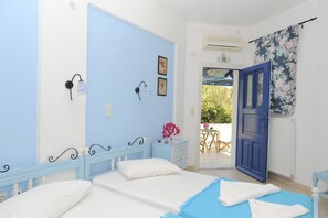 A bedroom with two beds, a blue door, and a view of an outdoor area. - Dora's Studios and Apartments (Syros)