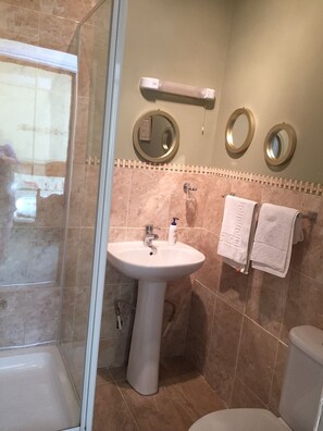 A bathroom with a pedestal sink, two wall-mounted mirrors, a towel rack with white towels, and a shower area with a glass door. - Church View B&B and Holiday Cottages (York)