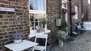 A brick building with a sign reading "OUR HAPPY PLACE" and another sign "IN THE GARDEN". There are outdoor seating areas with tables and chairs, and potted plants around. - Church View B&B and Holiday Cottages (York)