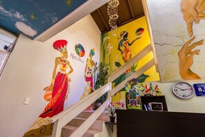 A staircase with colorful murals, a clock, and a chandelier. - Hotel das Palmas (Florianópolis)