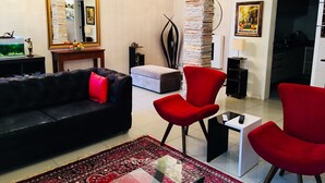 A living room with a black sofa, red chairs, a glass coffee table, and a patterned rug. - Hotel das Palmas (Florianópolis)