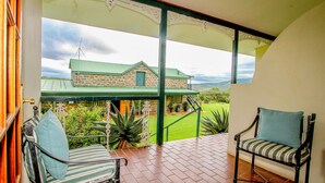 A balcony with two chairs, a stone building in the background, and a view of the landscape. - SpionKop Lodge (Ladysmith)
