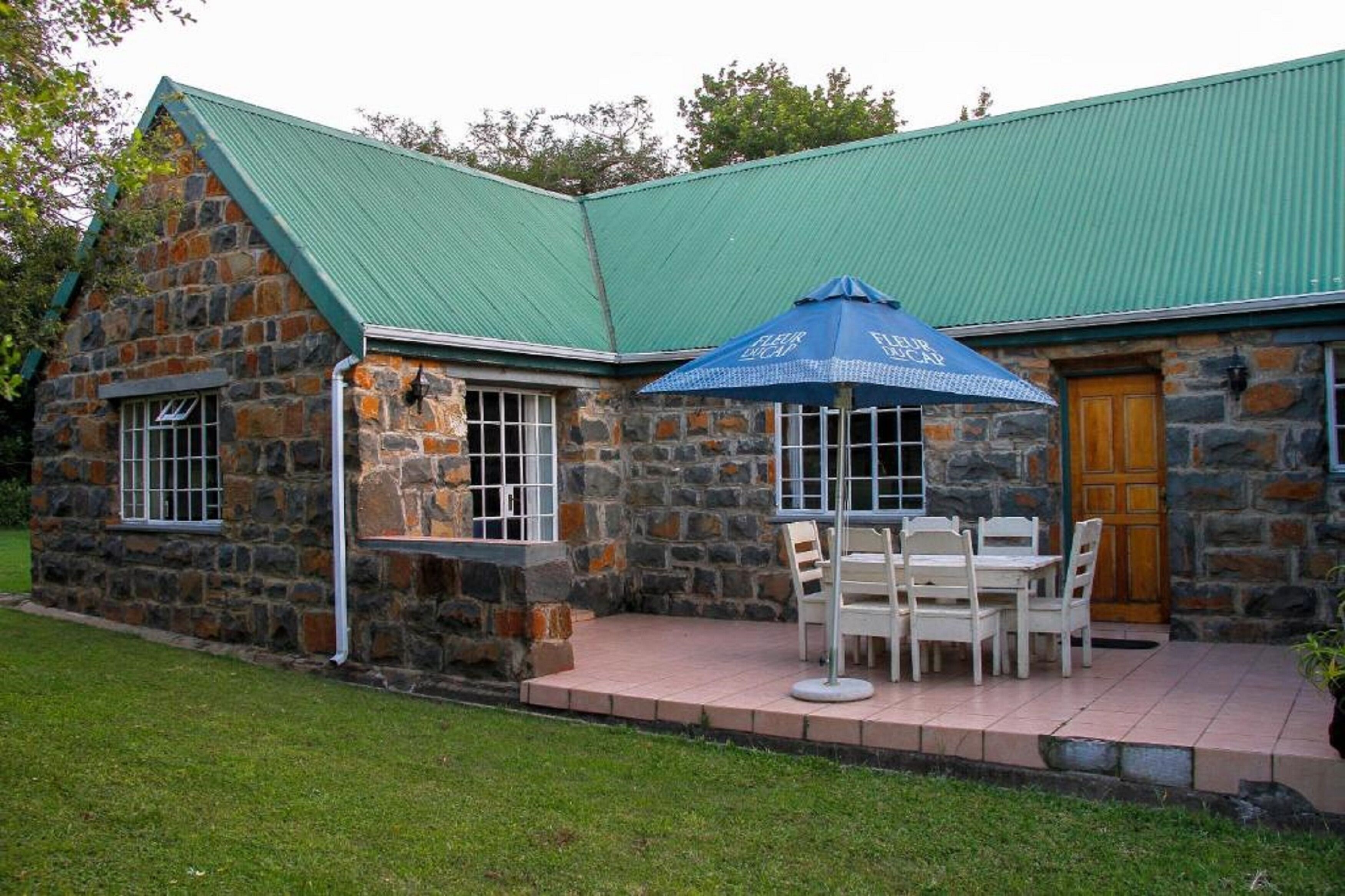 A stone building with a green roof, a wooden door, and a patio with a table and chairs.