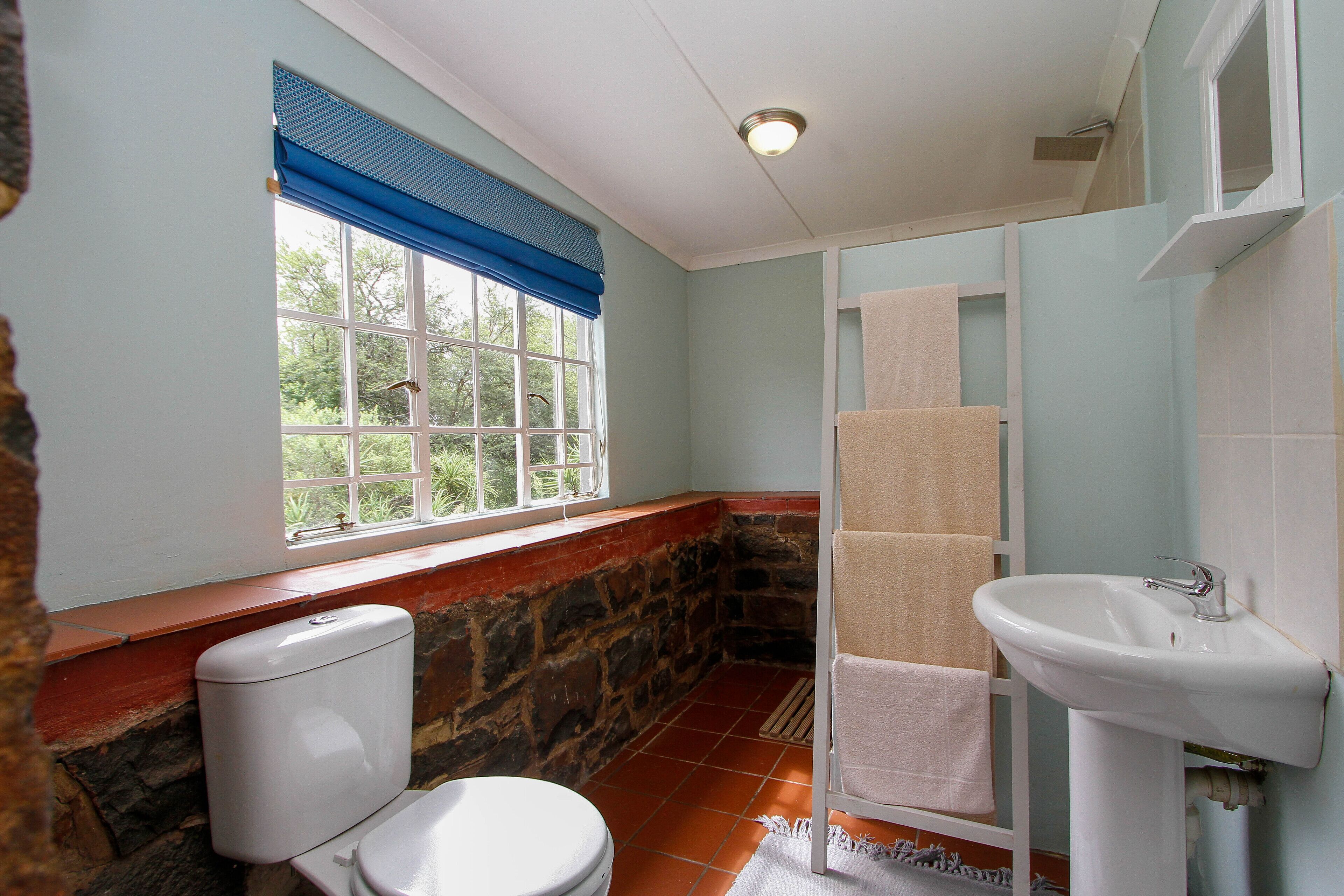 A bathroom with a stone wall, a white toilet, a sink, and a window with blue blinds.