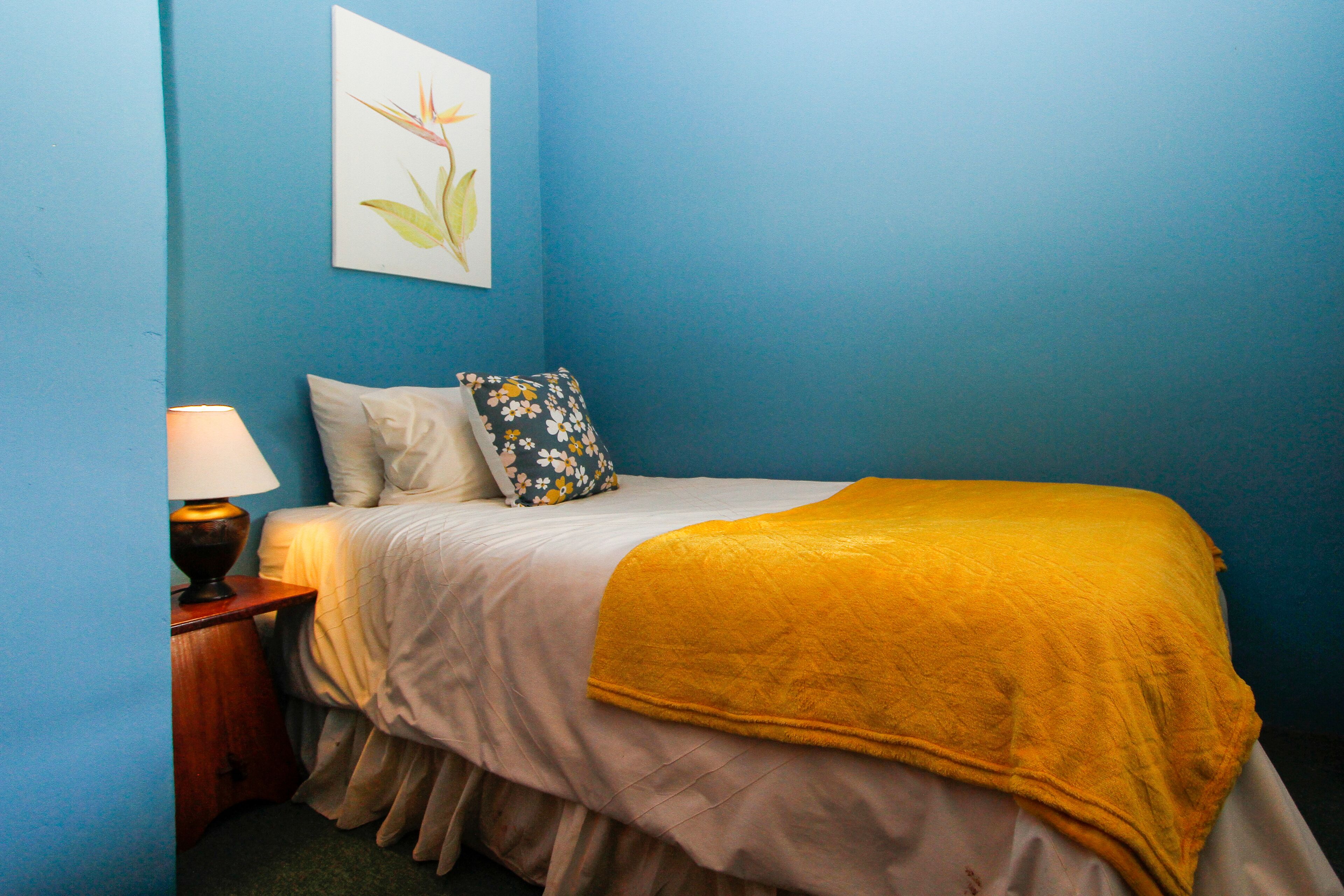 A bedroom with a bed, a nightstand, a lamp, and a floral pillow.