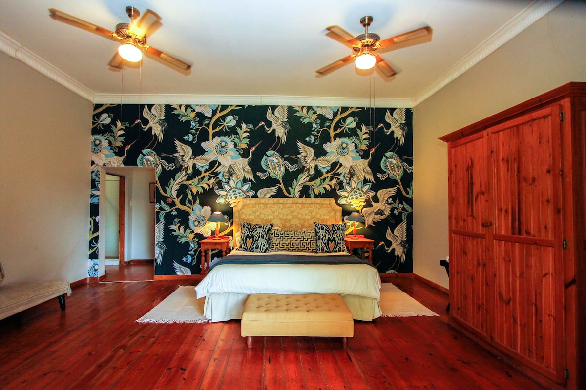 Quarto com cama grande, duas mesas de cabeceira, um guarda-roupa de madeira e um ventilador de teto.