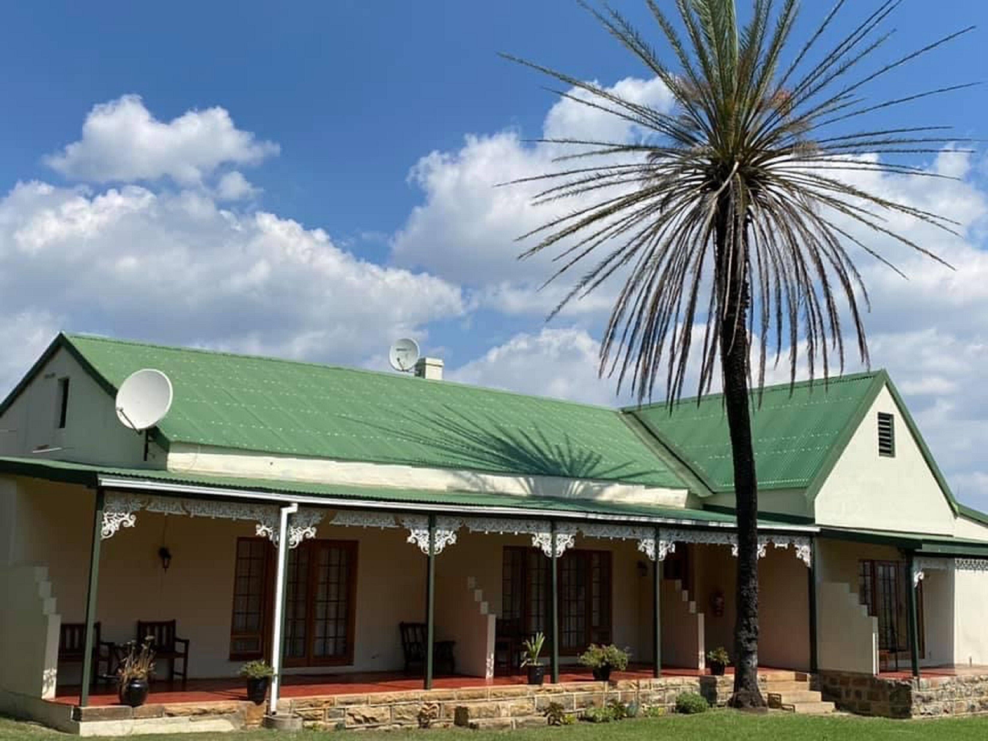 Une maison à deux étages, dotée d’un toit végétalisé, de murs blancs et d’un porche orné de motifs en dentelle.
