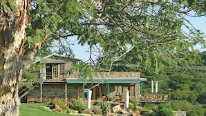 A stone house with a green roof, surrounded by a well-maintained lawn and a large tree. - SpionKop Lodge (Ladysmith)