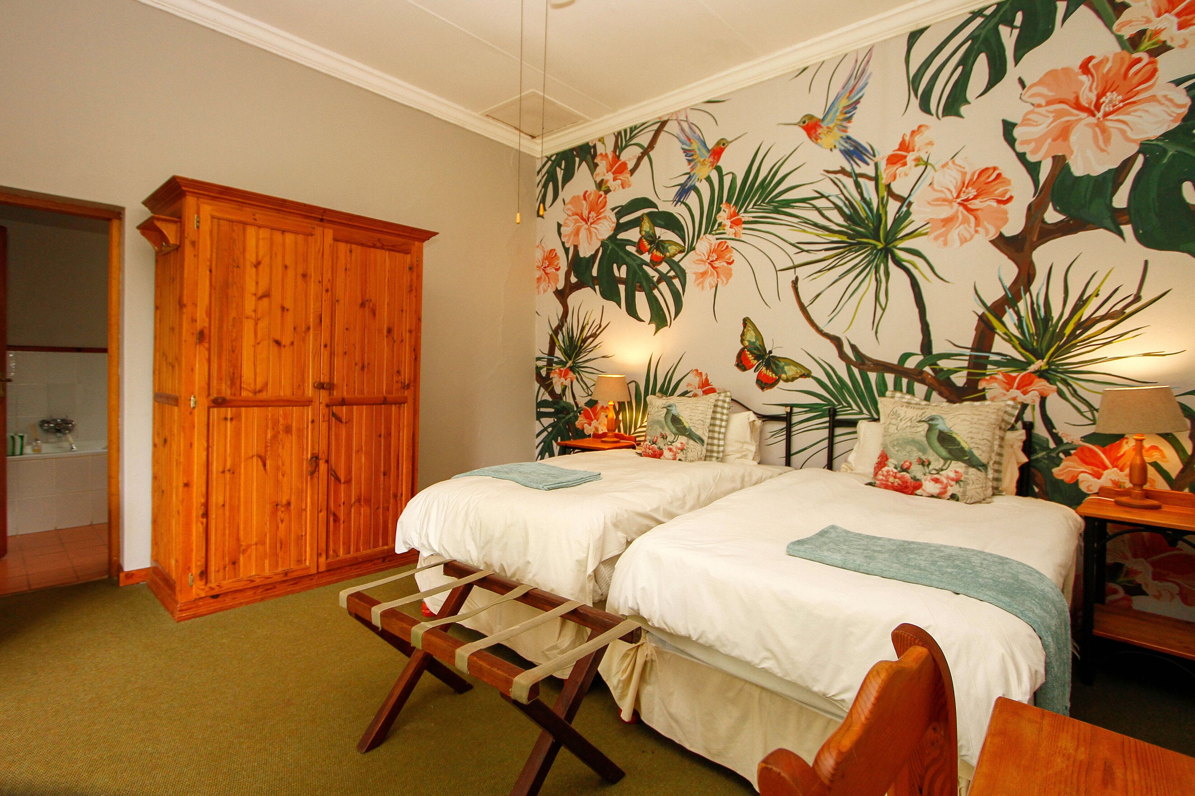 Un dormitorio con dos camas, un armario de madera, un mural temático de la selva tropical y una mesita de noche con una lámpara.