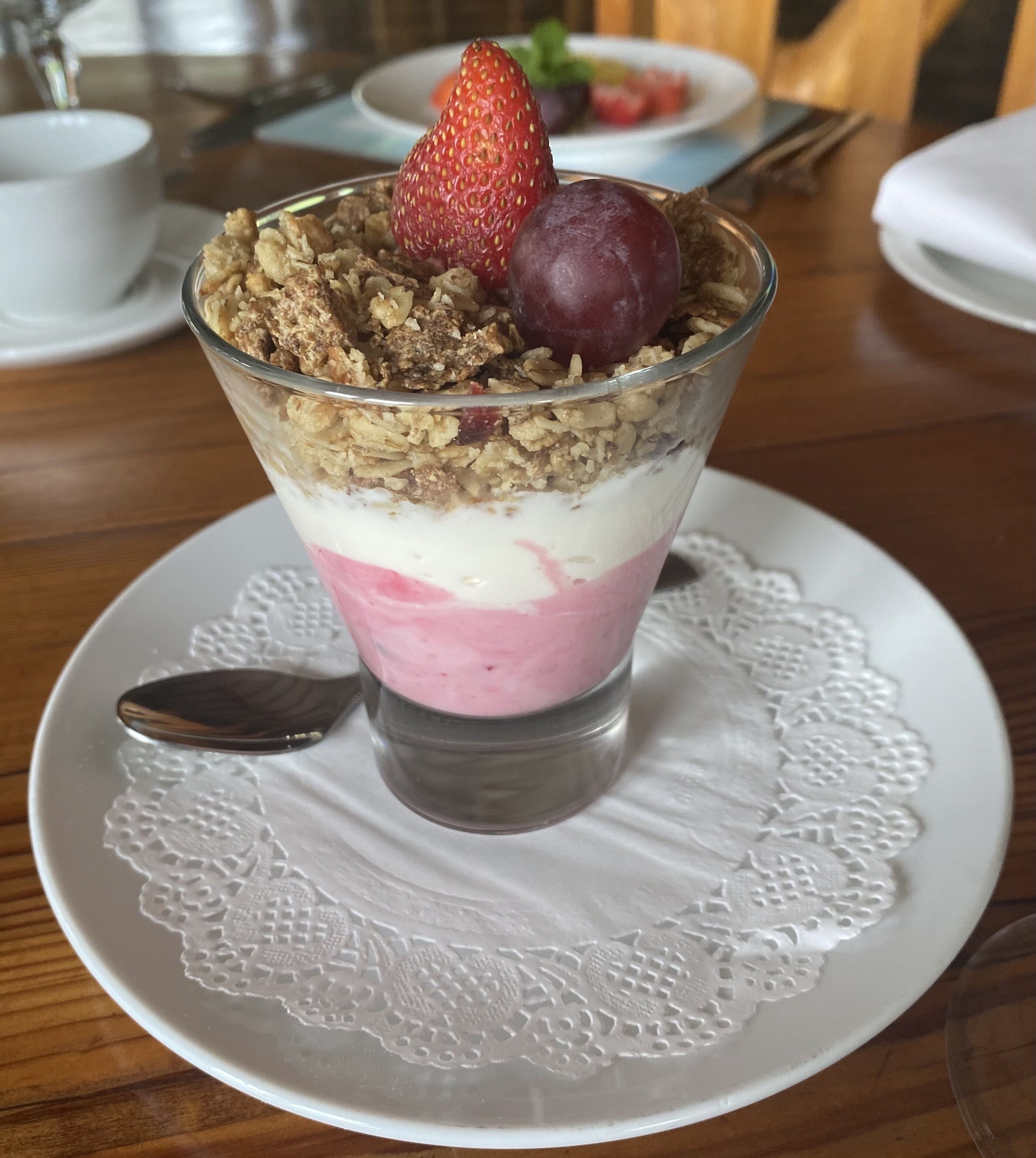 Un postre en una copa de vidrio sobre un plato blanco, con una cuchara.