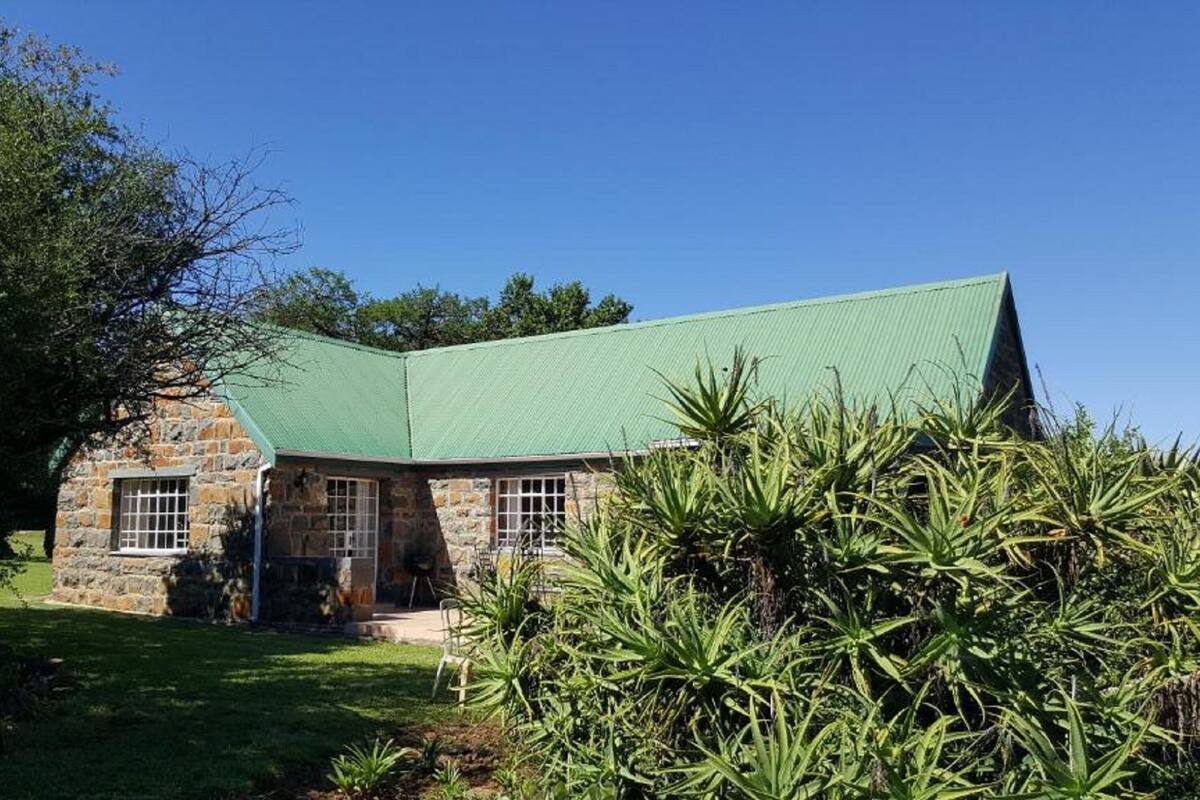 Uma casa de pedra com telhado verde e uma pequena varanda frontal.