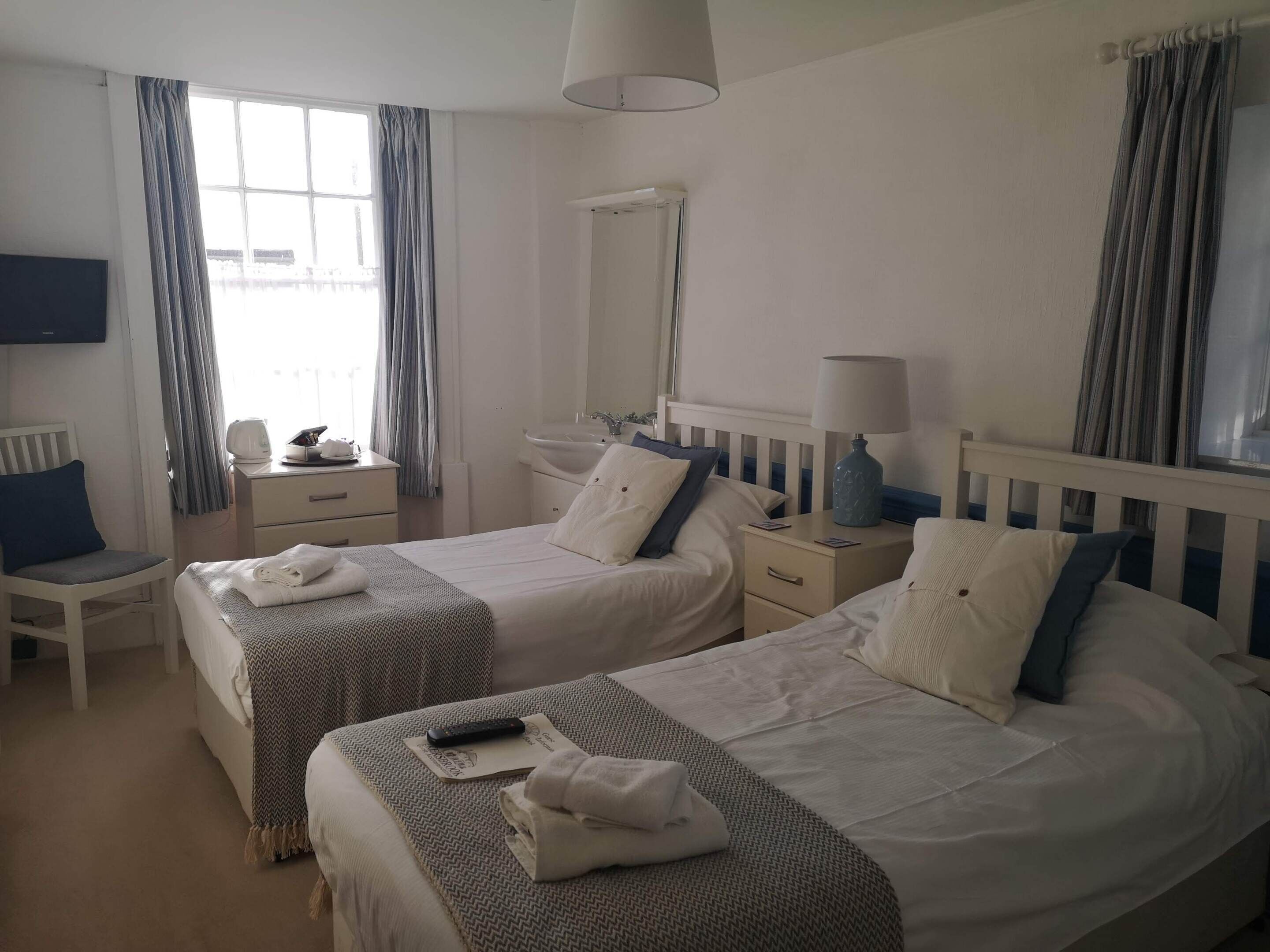 A hotel room with two beds, a desk, a chair, a TV, a lamp, and a window with curtains.